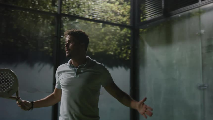 A man playing tennis on a court at night acting aggressively