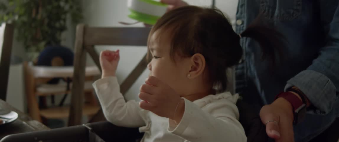 Pregnant mother with denim jacket and white top brings a bowl of baby food for toddler daughter sitting at table