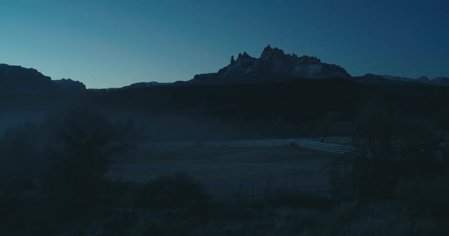 Fog lingers at dawn over a ranch at the base of prominent desert mountains