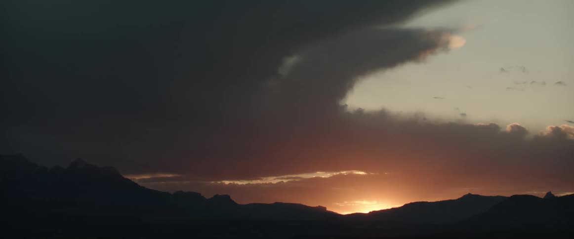 The sun rises on the mountainous horizon as dark clouds loom in the sky above