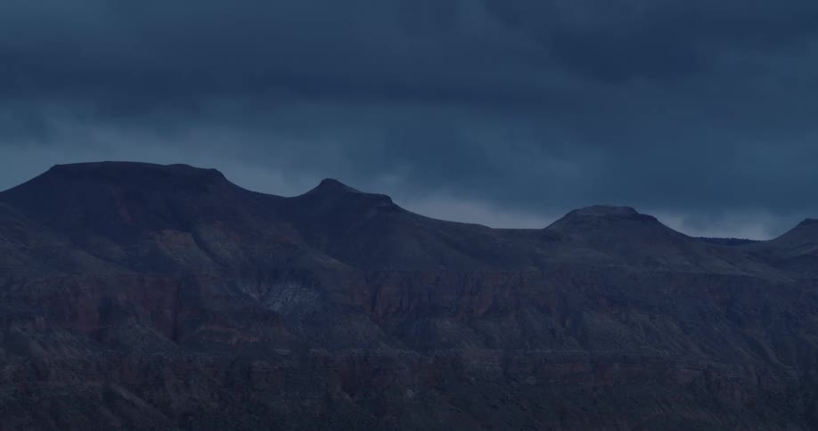 Landscape of barren desert ridges and mountains under stormy clouds at dusk