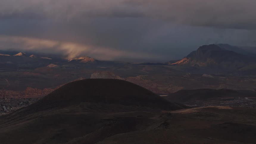 Aerial view of rolling desert hills and mountains during a stormy sunset