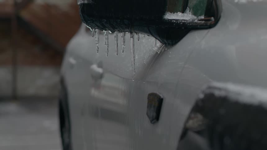 Close up of the rearview mirror on a white car parked outdoors covered in icicles at winter