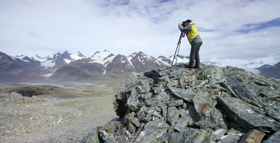 A photographer standing on a rocky peak is taking a photograph