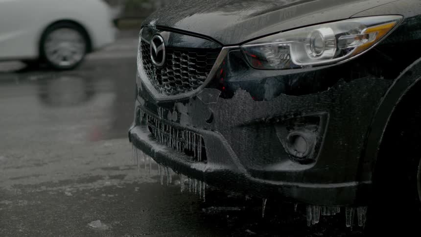 Ice covers the front of a vehicle parked on a street during the day