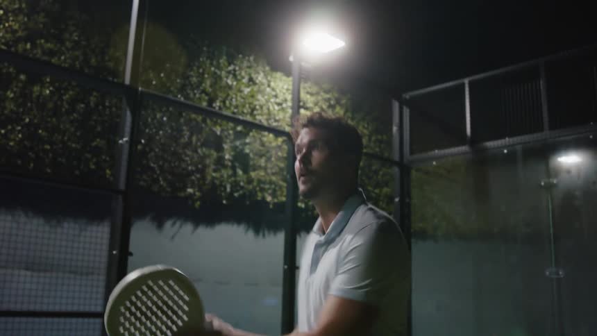 Man with polo shirt plays tennis on the tennis court at night