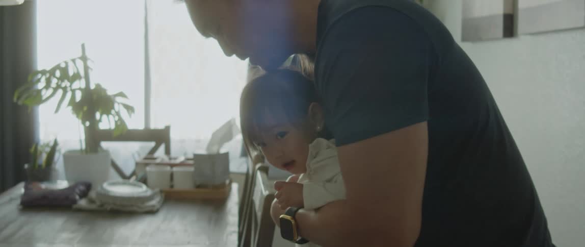 Father tries to sit his daughter in her highchair at the dining table