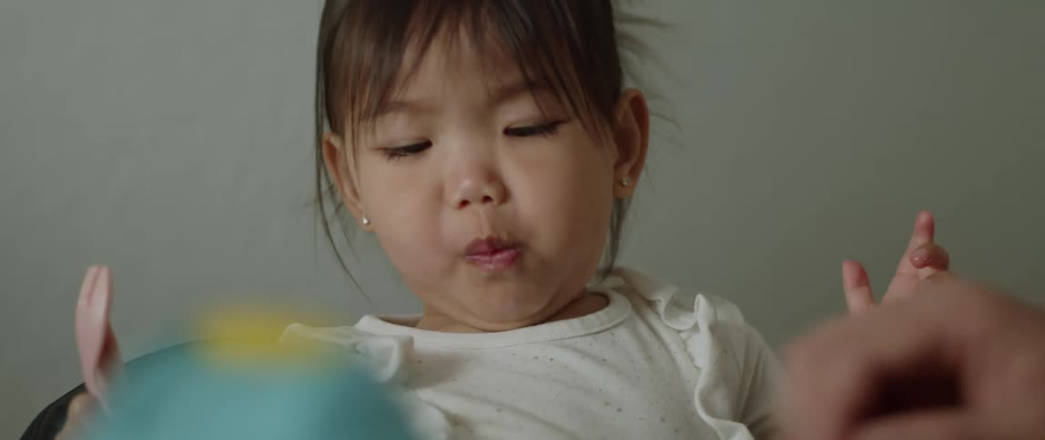 Little girl sitting eating food with her hand holding a plastic fork in the other hand