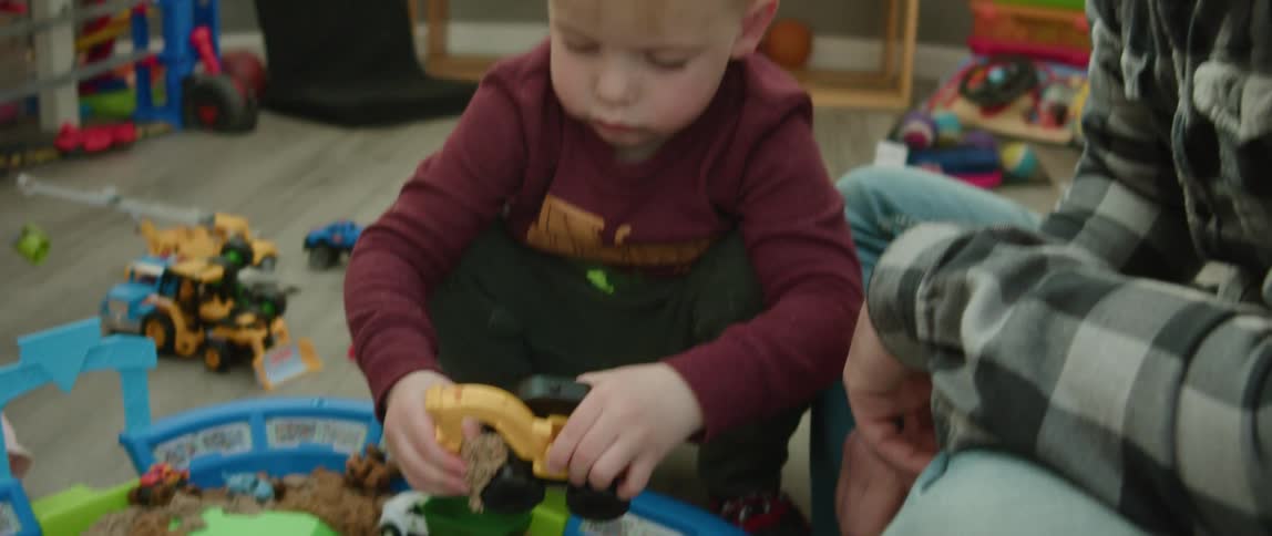 Young boy plays with a plastic toy excavator on a playroom with his father