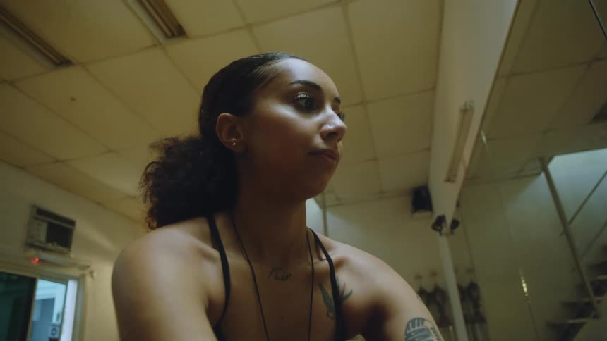 Close up of the face of a young woman wearing sports clothes sitting on the floor of a gym