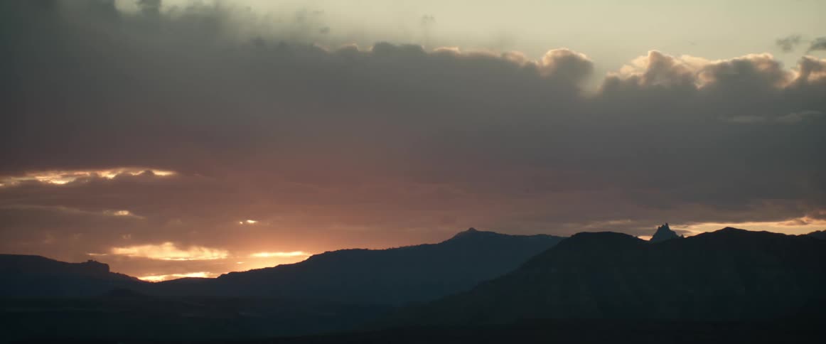 Thick clouds loom over a mountain range at sunrise