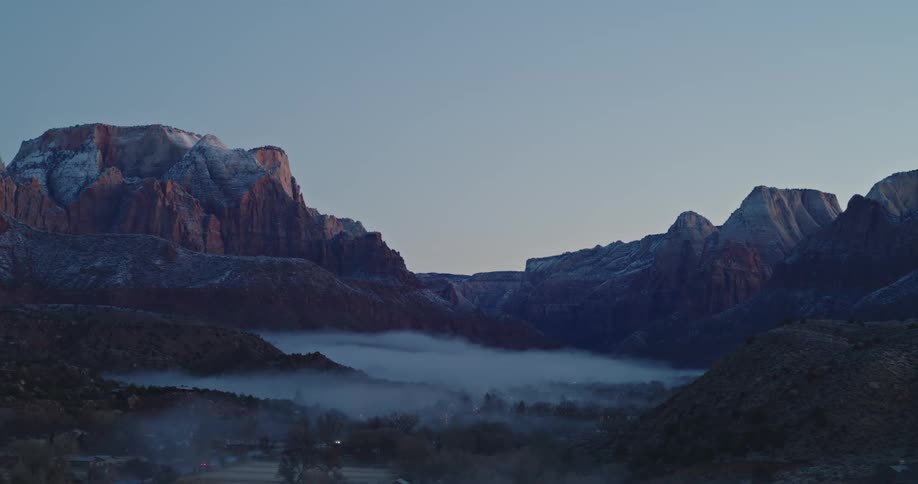 Foggy desert valley surrounded by snowy mountains at dawn