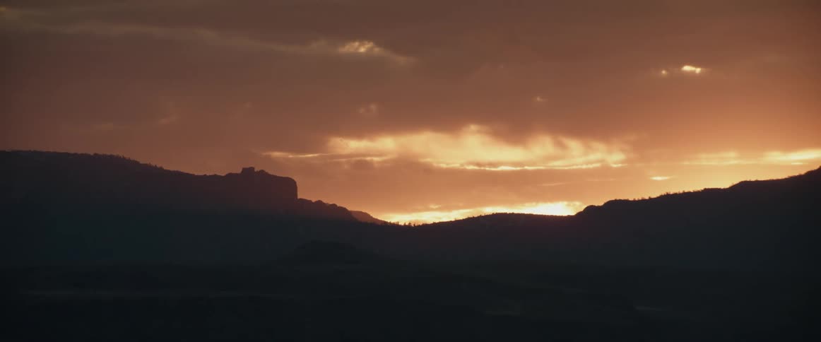 Silhouette of desert mesas and mountains in the badlands at dawn as camera zooms out
