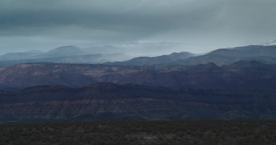 Distant mountain range towers over desert scrubland under a stormy sky