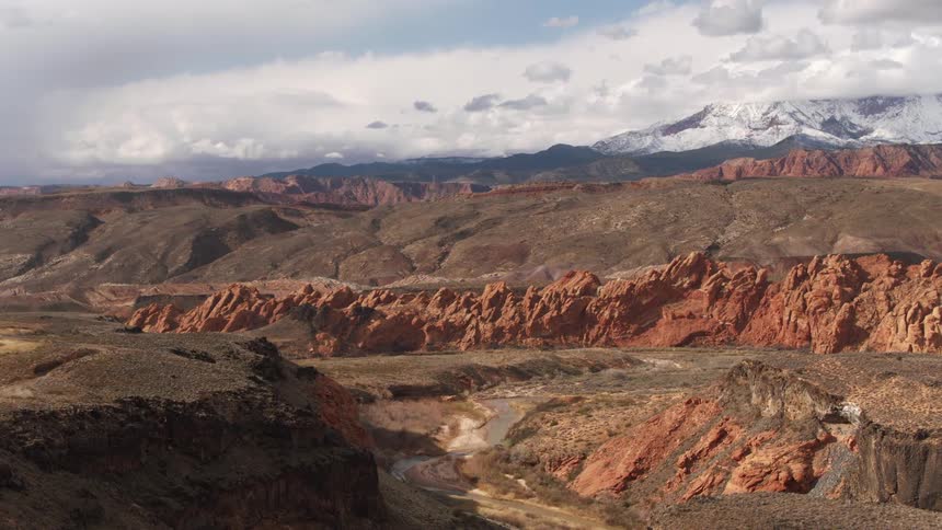 Aerial view of a desert river etching it's way through red rock canyons and distant snowy mountains