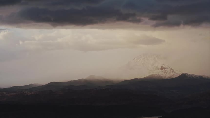 Aerial view of dark clouds snowing on a distant mountain