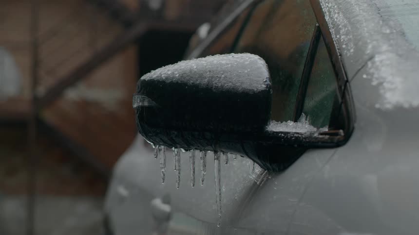 Icicles hanging off a rearview mirror on a car in the winter