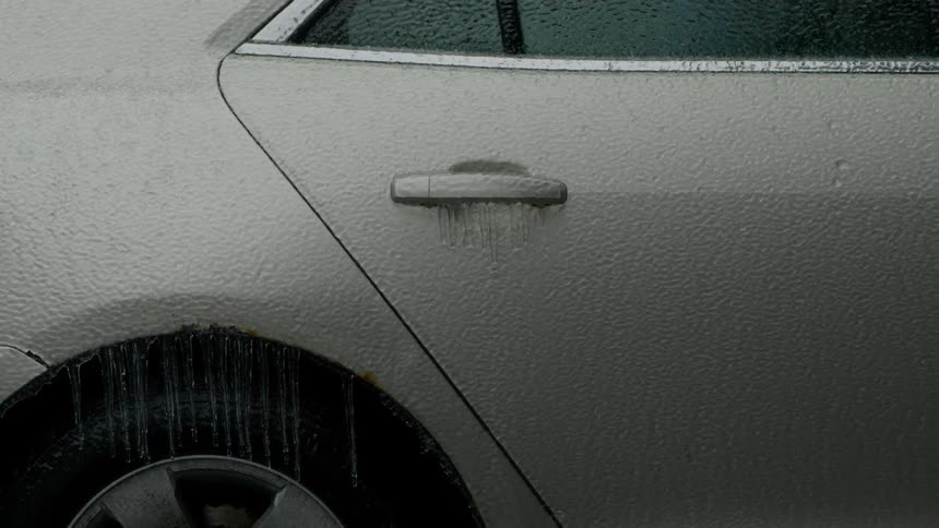 A beige colored car is parked still covered in rain drops