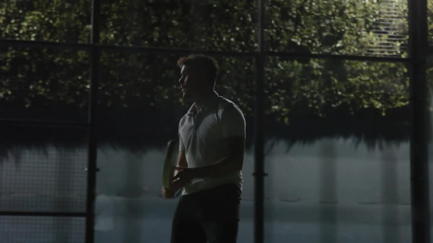 A man playing tennis in a glass room moving back and forth on the court