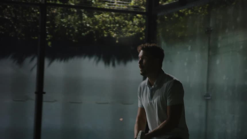 Young active man playing squash on an indoors court at night