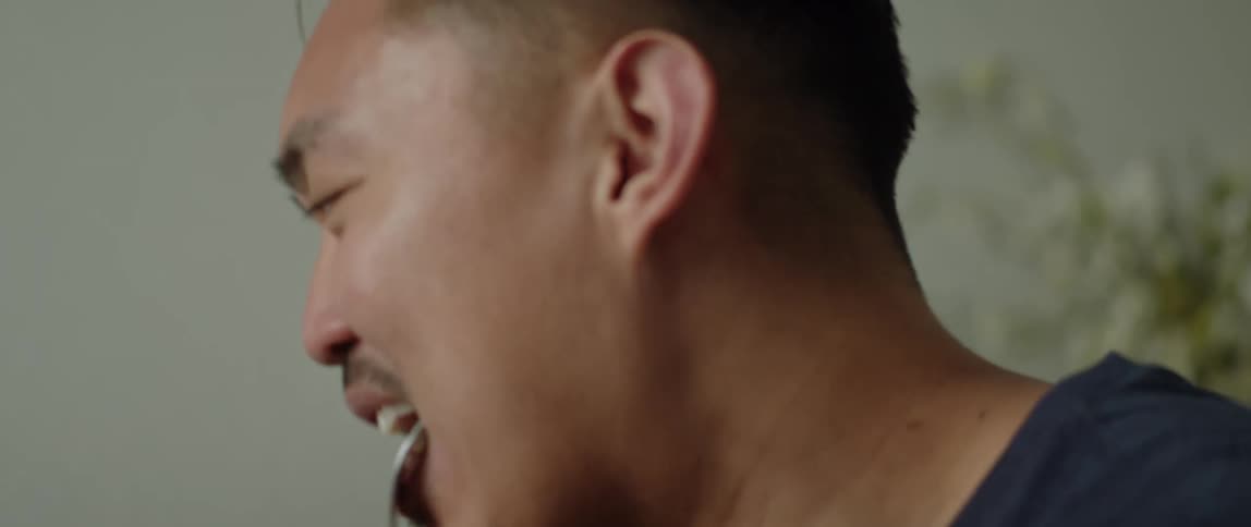 Man with dark blue t-shirt eats food and laughs