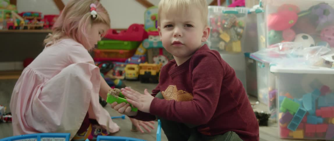 A boy and girl play with block toys and sand in a room filled with toys