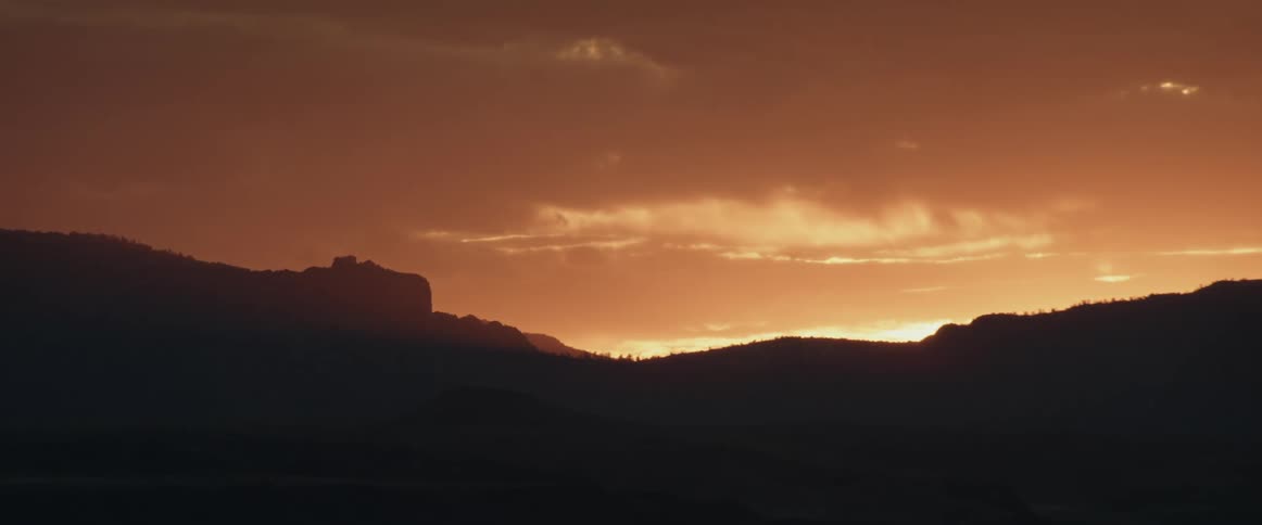 The morning sunrise glows through clouds over the desert mountains