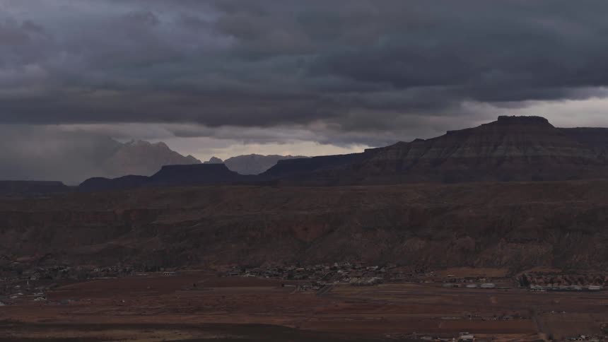 A small town seen in the desert under dark storm clouds and distant rain