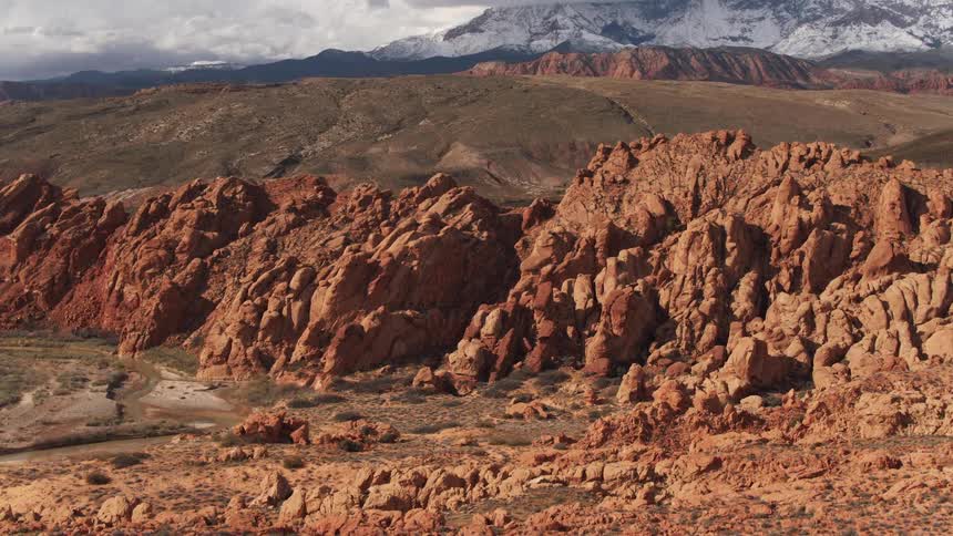 Aerial view of the desert red rock formations in front of mountains in the badlands