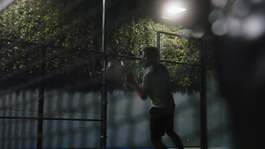 A man playing tennis on an outdoor court at night