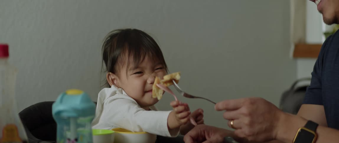 Father and daughter sitting at table eat food and laugh together