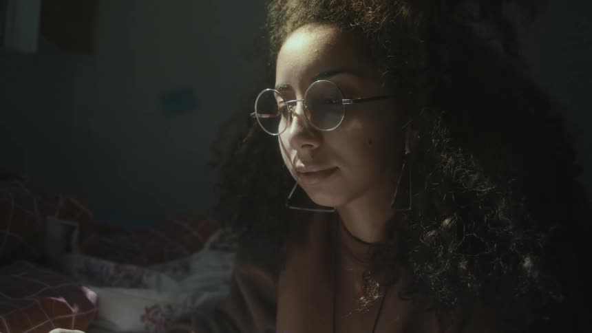 Woman with brown sweater glasses and curly hair reads a book