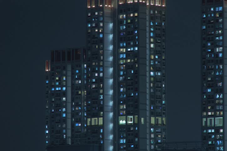A time lapse of tall symmetrical buildings in a city at night with shining lights turning off through the windows