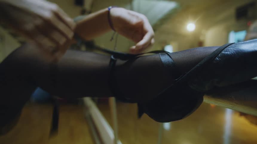 Woman standing in ballet studio with leg up on barre lacing up ballet shoes