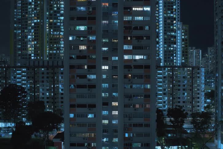 The windows of apartment towers in a city light up and turn on at night