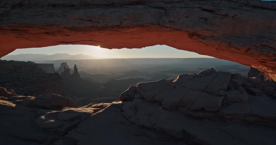 The sun appears underneath a glowing red rock arch in the morning