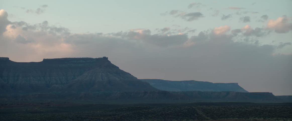 The camera zooms in on desert mesas and ridge formations at sunrise