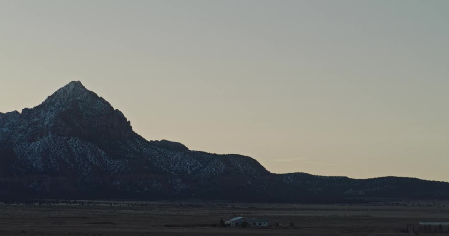 A farm house sits alone in the desert with a looming mountain seen behind
