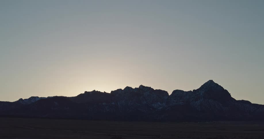 A silhouette of a mountain range with the sunlight shining over the peaks