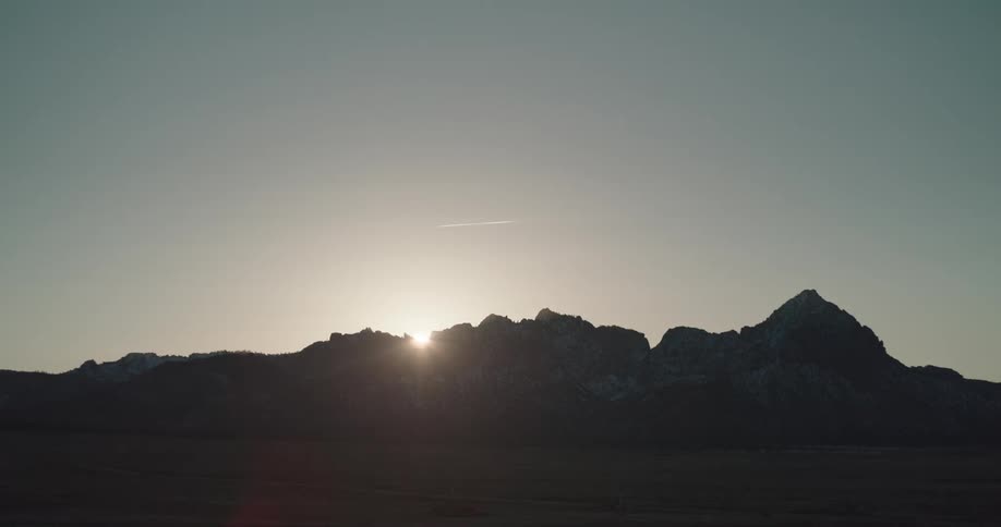 Sun peeks over the silhouette of a mountain range in the desert at dawn