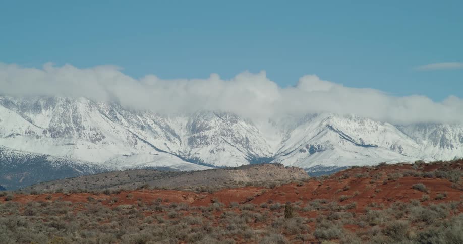 Fresh snow covers distant mountains with the red desert visible