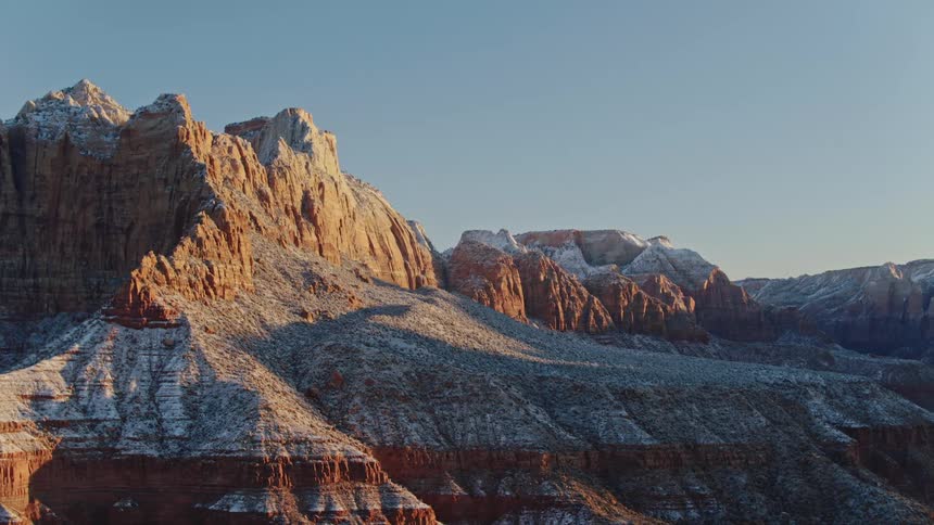 The sun shines upon snowy red rock mountains in the desert under a clear blue sky