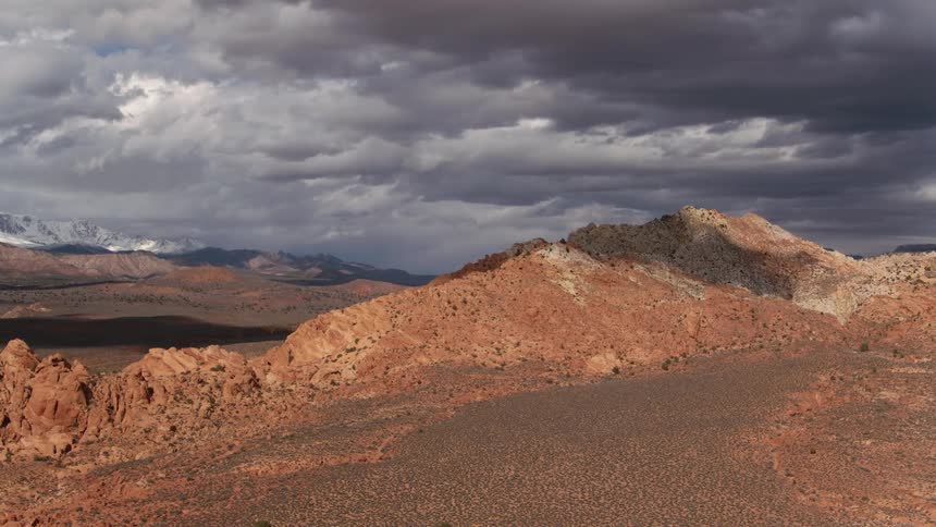 An aerial view of a rugged red rock mountain with shifting sunlight
