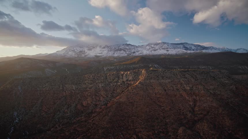 Aerial view of the snow covered peaks of a red rock mountain range at sunset