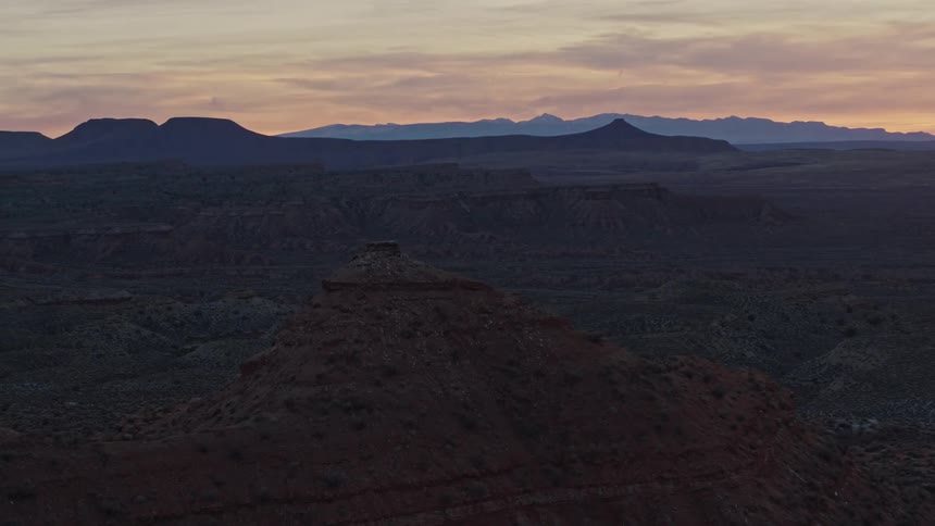 Aerial view of eroded mesa peak with distant desert mountains at dusk