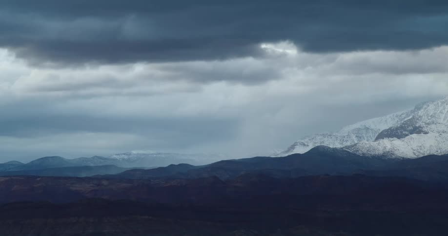 Dark clouds move over a snow covered mountain range at dusk