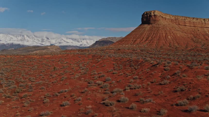 An aerial view of a desert plain with distant red cliffs and canyons