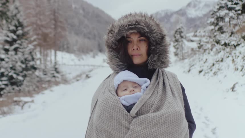 A mother wearing a fur winter jacket carries her baby on a snowy road