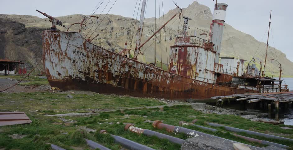 A rust covered boat sits on land