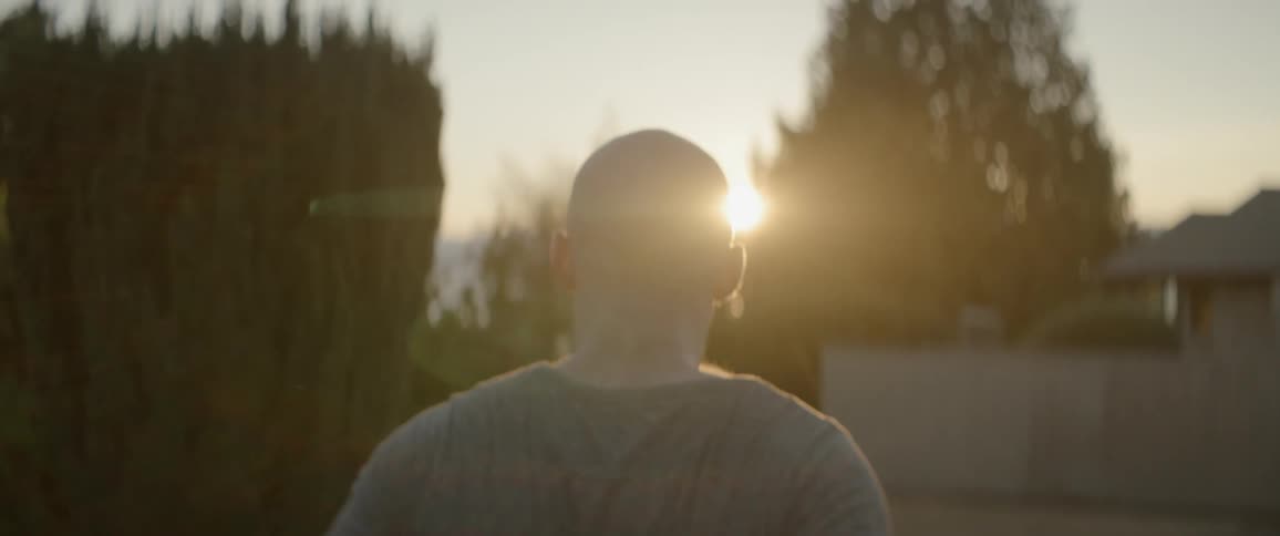 A man stands looking at the sun setting in the distance between trees